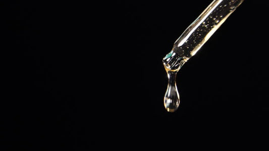Golden beard oil drop falling from a glass dropper against a black background